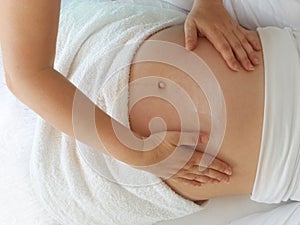 Close to the female hands of a massage therapist makes a light massage to the belly of a pregnant girl in a cosmetology room