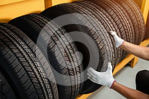 Close to the hands of a tire changer in Large warehouse of car tires, rack with customer car tires in warehouse of a tire dealer