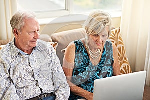 Close to home and to the outside world. a senior couple using a laptop together on the sofa at home.