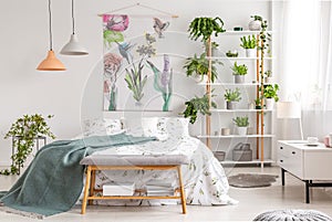 Close to nature bright bedroom interior with a bed covered with white sheets and marine blanket. Green plants on shelves next to t