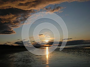 Evening sky with dark rainclouds and fiery sunlight reflections at Findhorn Bay, Scotland