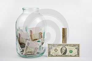 Close to three-liter jar filled with money is a stack of coins next to it is a banknote of ten dollars