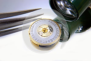 Close uo of a watch movement with tweezers and a magnifying monocle