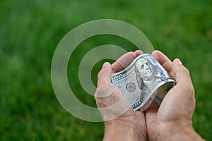 Close up 100 Dollar bank note in hand on grass background. One hundred American dollars.