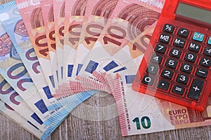 a Close-up of 20 and 10 euros lying fanned out on a wooden table with a red calculator