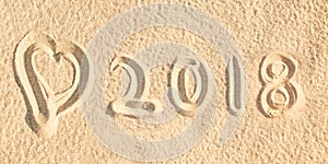 Close up on 2018 written in the sand of a beach wih a heart