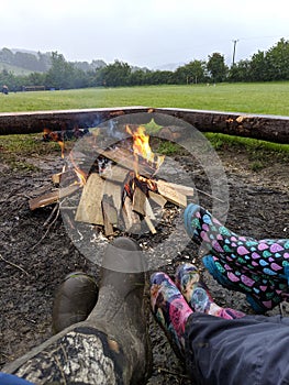 A close up of 3 people in pairs of Wellington boots sitting around a campfire