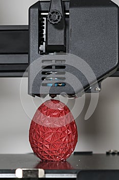 Close up of a 3d printer printing a red polygonal egg