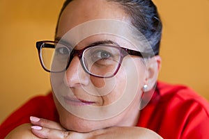 Close up of a 45 to 50 year old woman wearing glasses and dressed in red with a relaxed, smiling and self-confident expression.