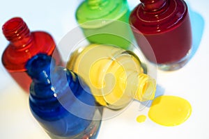 Close up of 5 open bottles of nail polish blue, red, dark red, green, yellow isolated on white background. Open yellow bottle lay