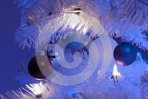 Close up of 5 ornaments in white christmas tree with white light in foreground and blue lights in background