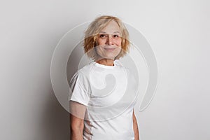 Close up of a 60s middle age woman smiling and wearing a white t-shirt on a white studio wall background