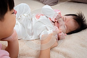 Close-up of a 9-year-old boy playing in bed with 3-month-old newborn sister. An Asian boy takes care of his sister in soft bed in