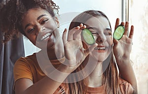 Close up above photo of two best girlfriends spending time together having fun while applying cucumber slices on eyes holding them