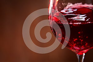 Close-up of the abstract splashing of the red wine in the fragile wineglass on the brown wooden background.