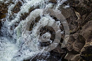 Close-up abstract texture above view of river torrent and clear fresh cold water flowing through mountain rocks in valley with