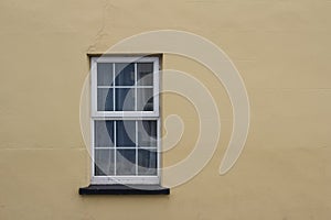 Close up abstract view of a white window surrounded by an smooth yellow solid wall texture