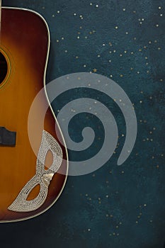 Close up of acoustic guitar and carnival mask on blue background with glitter photo