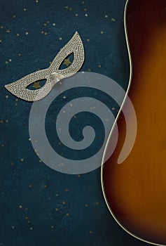 Close up of acoustic guitar and carnival mask on blue background with glitter