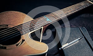 Close-up, acoustic guitar and notepad on a dark background.