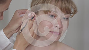 Close-up of acupuncturist checking points in ear of young Asian woman. Process of auriculoacupuncture. Alternative