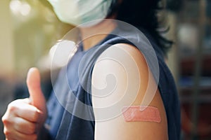 Close-up adhesive bandage on unrecognized person`s arm after injection of vaccine, people in face mask received a coronavirus