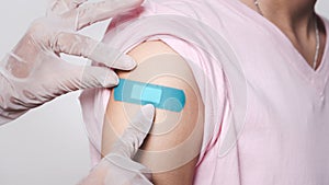 Close up adhesive bandage on woman arm after injection vaccine, medical doctor putting plaster while rubber protective gloves