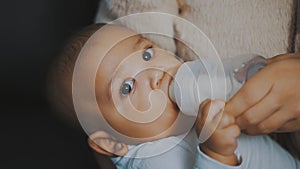 Close up adorable dark skin baby drinking his milk from the bottle in mothers hands