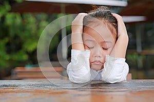 Close-up of adorable little Asian child girl expressed disappointment or displeasure on the wood table