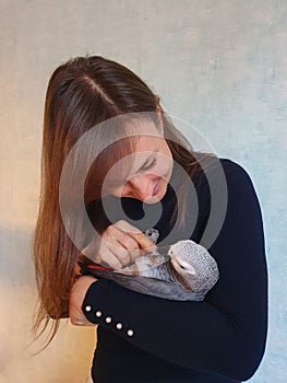 CLOSE UP: Adorable shot of a young woman cuddling with her friendly grey parrot.