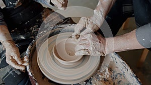 Close-up of adult and child`s hands making ceramic bowl from clay on pottery wheel