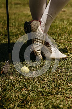 Close-up of an adult female standing on a lush, green grassy field with golf ball near the shoes