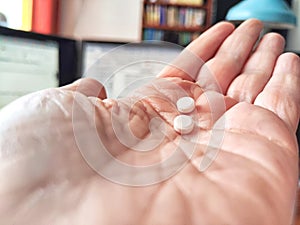 Close-up of an adult hand holding two small white pills. Close-Up of Two Pills in an Open Palm Indoors