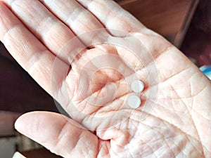 Close-up of an adult hand holding two small white pills. Close-Up of Two Pills in an Open Palm Indoors