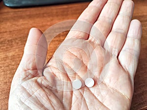 Close-up of an adult hand holding two small white pills. Close-Up of Two Pills in an Open Palm Indoors