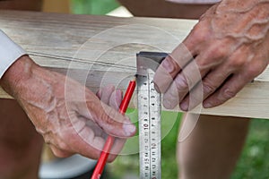 Close-up of adult male hands holding woodworking marking tool - red pencil and metal ruler corner and measures and marks the area