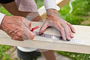 Close-up of adult male hands holding woodworking marking tool - red pencil and metal ruler corner and measures and marks the area