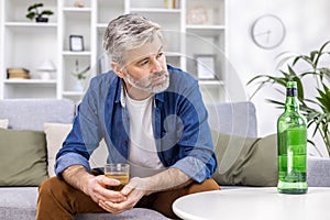 Close up of adult mature man lonely depressed drinking strong alcohol sitting on sofa in living room on day