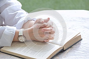 Close up of adult woman hands praying with open Holy Bible on octagon marble table in porch area at home