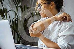 Close up of adult woman massaging her elbow for overwork writing on computer sitting at the desk in office home workplace. Concept