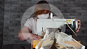 Close up of adult woman stitching curtain, using sewing machine. Young seamstress in medical mask working on sewing