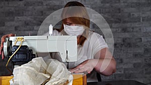 Close up of adult woman stitching curtain, using sewing machine. Young seamstress in medical mask working on sewing