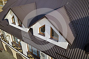 Close-up aerial view of building attic rooms exterior on metal shingle roof, stucco walls and plastic windows