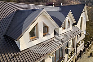 Close-up aerial view of building attic rooms exterior on metal shingle roof, stucco walls and plastic windows