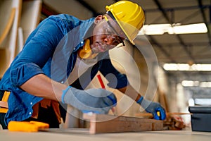 Close up African American carpenter man use pencil to mark on timber and work in factory for producing wood furniture or wood work