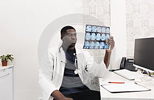 Close-up of an African-American doctor in a white coat looking at an X-ray image, CT, MRI,. Department of Radiology.