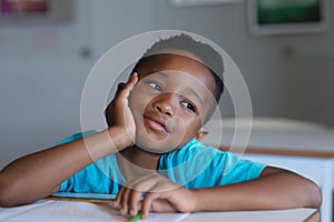 Close-up of african american elementary schoolboy looking away while leaning at desk in classroom