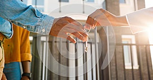 Close up of African American female hand passing key to male outdoors in sunlight. Woman handing keys of new house to photo
