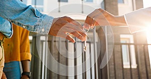 Close up of African American female hand passing key to male outdoors in sunlight. Woman handing keys of new house to