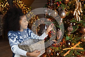 Close up African American girl decorating Christmas tree, holding basket